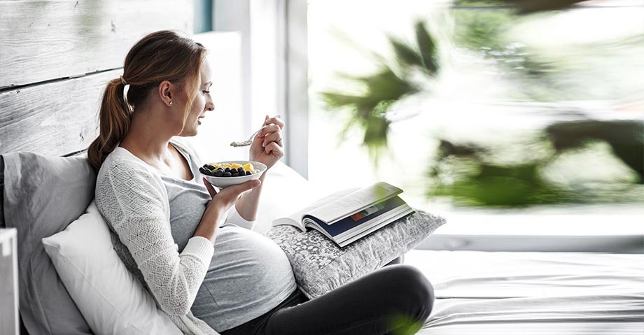 Kobieta w ciąży jedzące owoce i czytająca książkę - grafika pochodzi z bloga eksperckiego Boramed